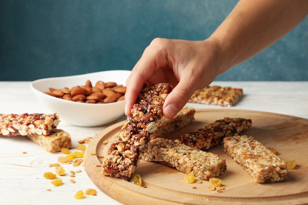 Make-Ahead Breakfast Ideas Female hand hold granola bar on wooden background with granola bars